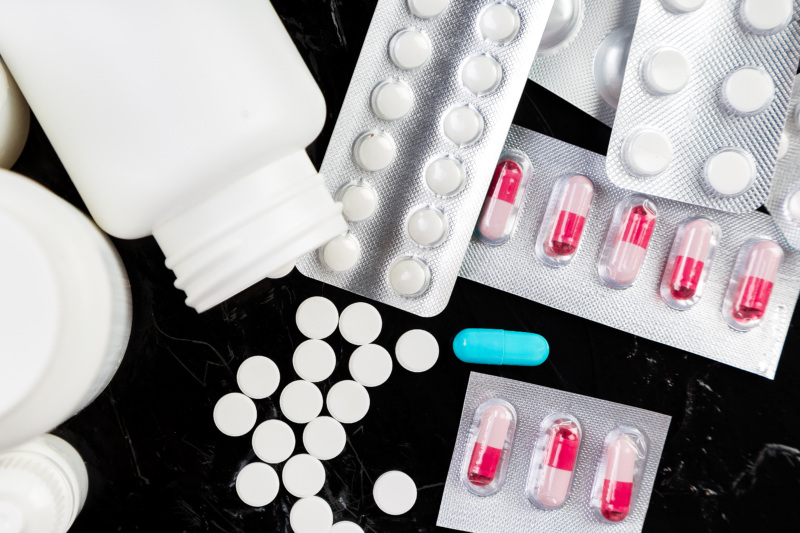 A variety of prescription pills and pill bottles displayed on a black surface.
